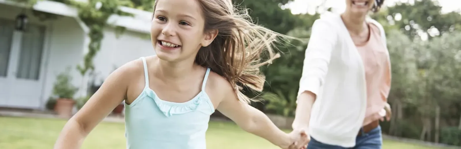Mother and daughter running through green yard