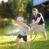 Dad chasing his son across yard with water hose