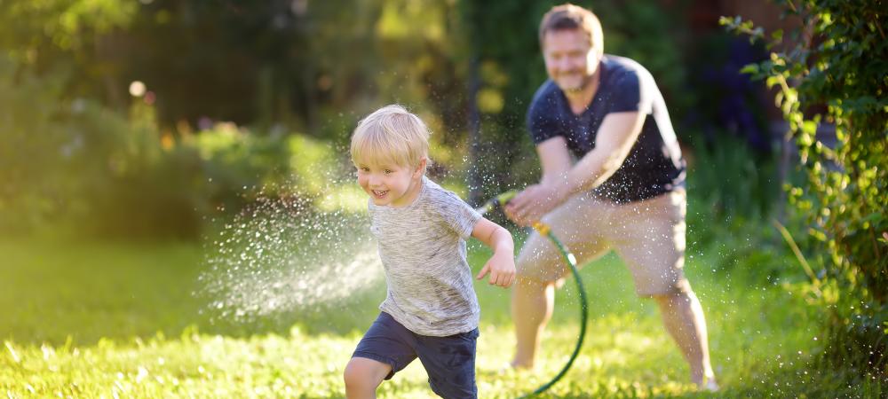 Dad chasing his son across yard with water hose