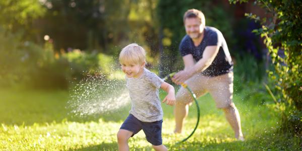 Dad chasing his son across yard with water hose